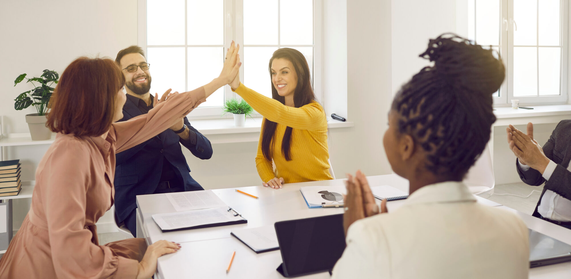 Happy women high five each other as they celebrate success during meeting with their business team